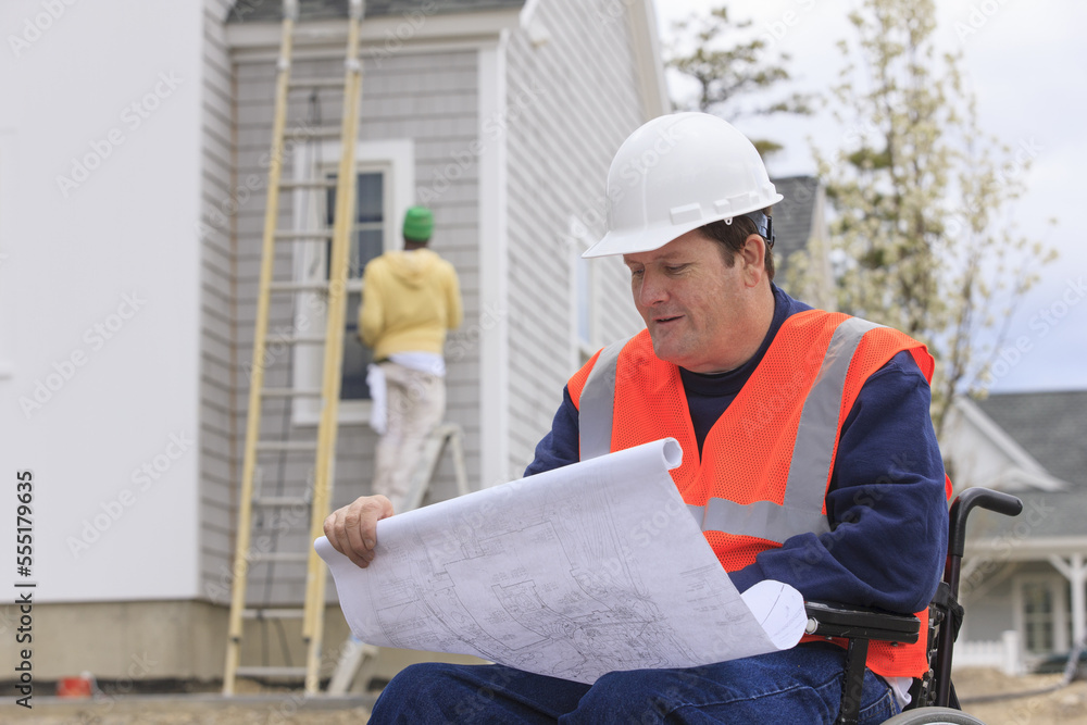 Construction engineer with spinal cord injury with house plans at construction site Construction engineer with spinal cord injury with house plans at construction site