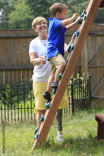 Grandmother with a prosthetic leg playing on an outdoor climber with her grandson photo