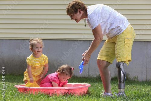 Grandmother with a prosthetic leg playing with her grandchildren on a child's pool photo