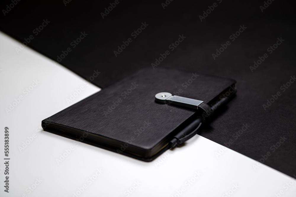 black organizer or notebook with pen on two-color black and white background, mockup, copy space black organizer or notebook with pen on two-color black and white background, mockup, copy space