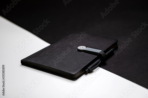black organizer or notebook with pen on two-color black and white background  mockup  copy space