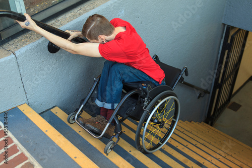 Trendy man with a spinal cord injury in wheelchair going down subway stairs backwards photo