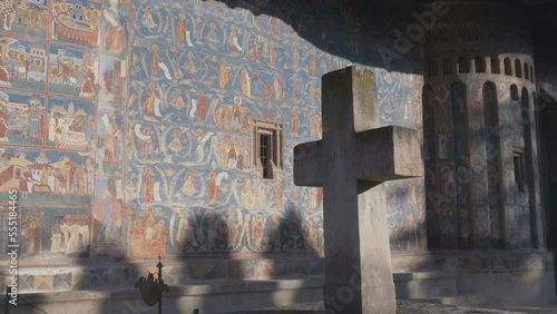 Stone cross and blue painted walls of Voronet monastery photo