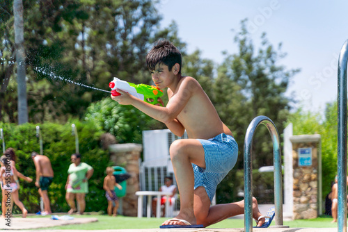 Dark-haired boy playing with the water gun in the pool