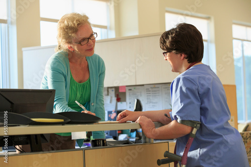 Nurse with Cerebral Palsy checking with administration about a patient's records in a clinic photo