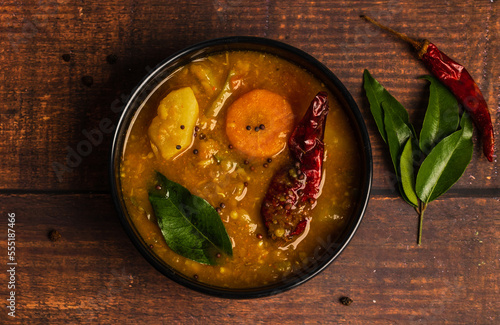Sambar, a mixed vegetarian curry arranged on a black bowl on a wooden background. Sambar is popular in South India and Sri Lanka cuisines.
