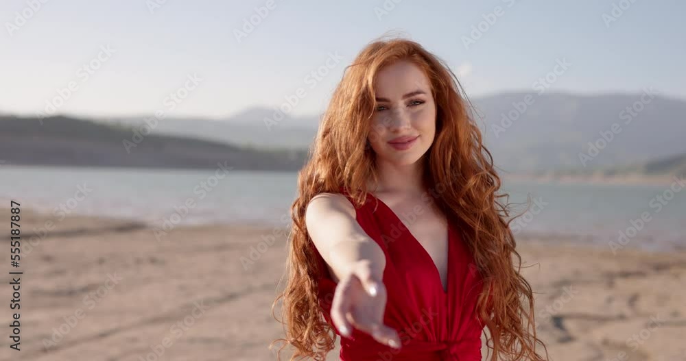 Redhead Female Wearing Red Dress on Beautiful Landscape Waving Hand, Inviting to Follow Her. Gorgeous Woman with Long Curly Hair Looking at Camera, Positively Smiling. Slow motion. Trust Concept Redhead Female Wearing Red Dress on Beautiful Landscape Waving Hand, Inviting to Follow Her. Gorgeous Woman with Long Curly Hair Looking at Camera, Positively Smiling. Slow motion. Trust Concept