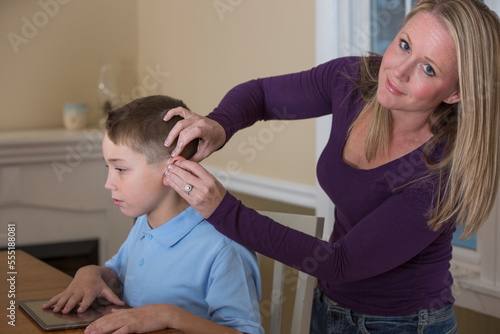 Mother putting a hearing aid on her son with a hearing impairment at home photo