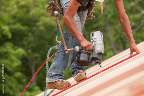 Hispanic carpenter using a nail gun on roof  panels