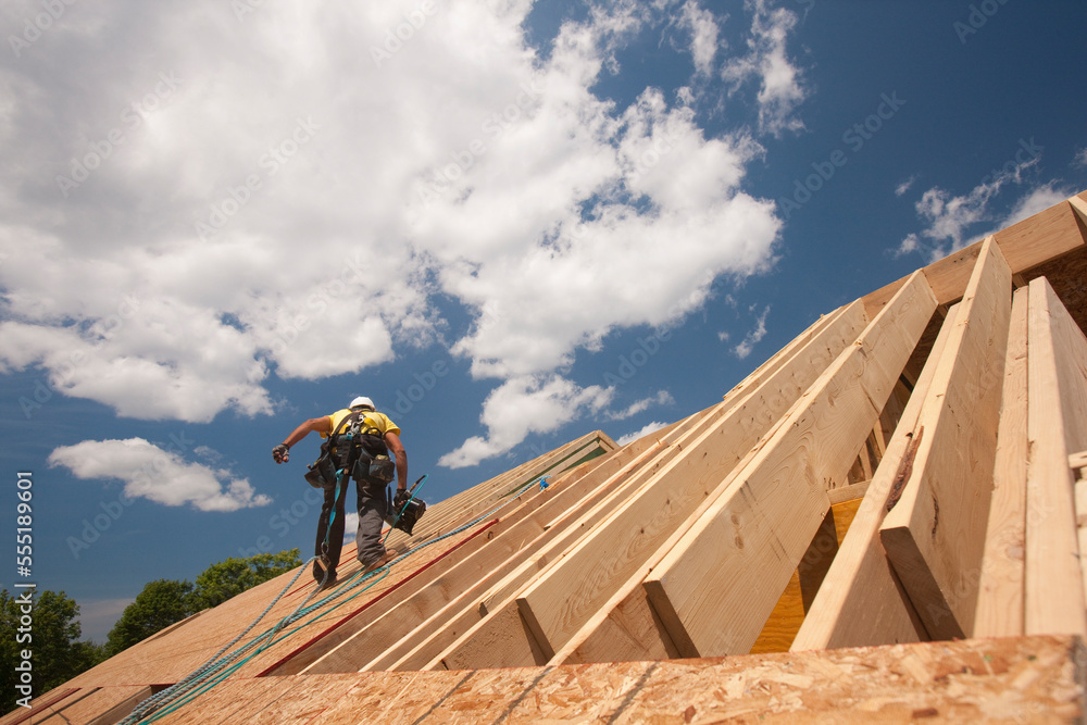 Carpenter holding a nail gun on the roof of a house under construction Carpenter holding a nail gun on the roof of a house under construction
