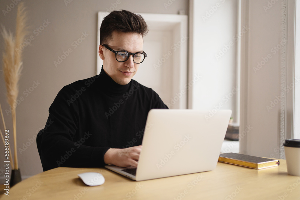 A young freelance man working at a workplace uses a laptop, prints an online text message. A young freelance man working at a workplace uses a laptop, prints an online text message.