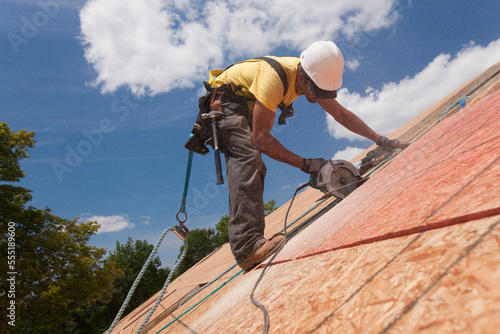Hispanic carpenter using a circular saw on a roof sheathing at a house under construction photo