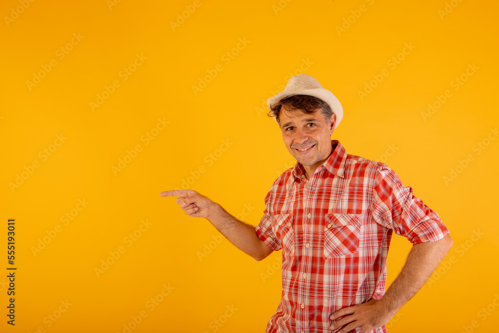 Man in hat and colorful checkered shirt pointing to the side with his hands on an orange background Man in hat and colorful checkered shirt pointing to the side with his hands on an orange background