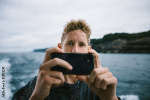 Blond teenage boy take a picture with his cell phone on vacation photo