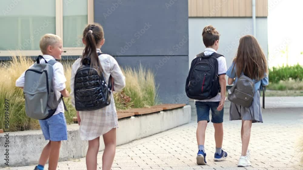 Four elementary school students, two boys and two girls, are walking around the school yard. The children are talking animatedly. Back to school.