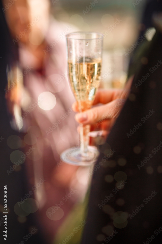 New Year's blurred festive background with a man's hand with a glass of champagne and bokeh from fireworks. wedding champagne party. the groom in a suit holds a glass of champagne in his hand. blurry