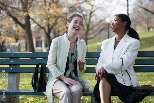 Two women sitting on a bench in the park and laughing. photo