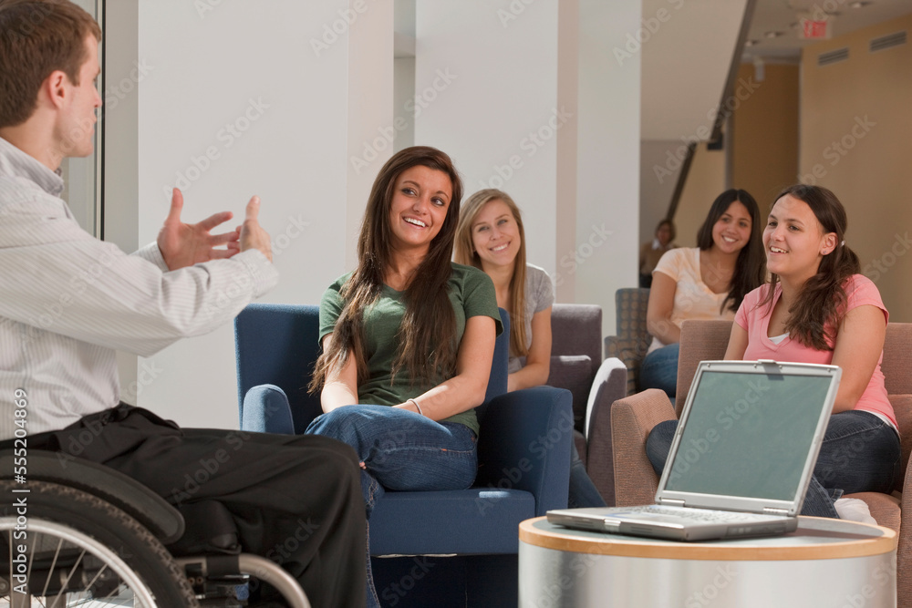 Teacher with spinal cord injury giving a lecture to students in classroom Teacher with spinal cord injury giving a lecture to students in classroom