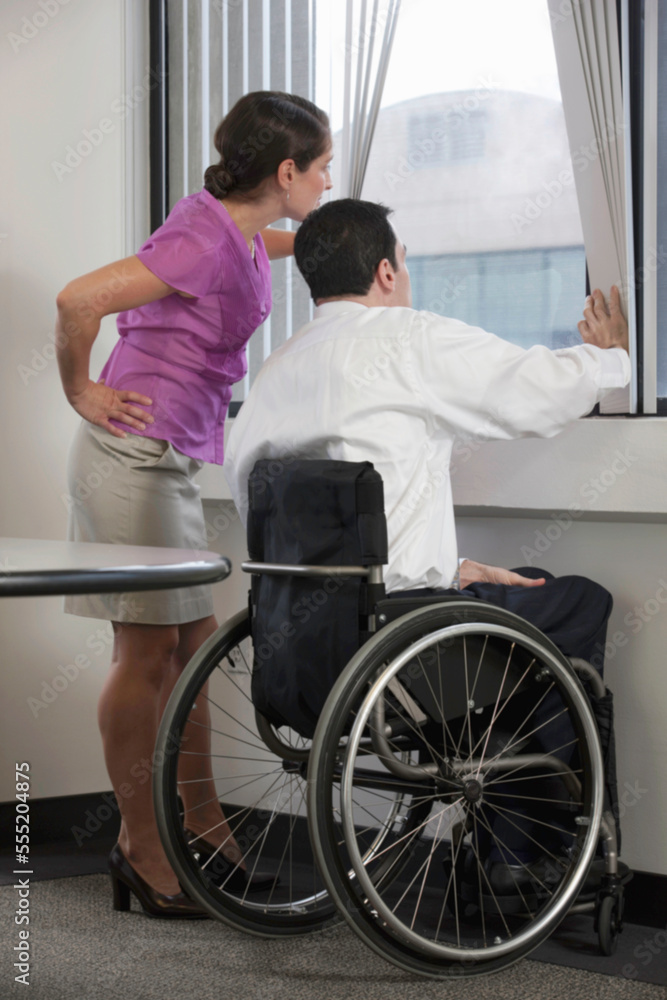 Businessman with spinal cord injury and a businesswoman looking through a window Businessman with spinal cord injury and a businesswoman looking through a window