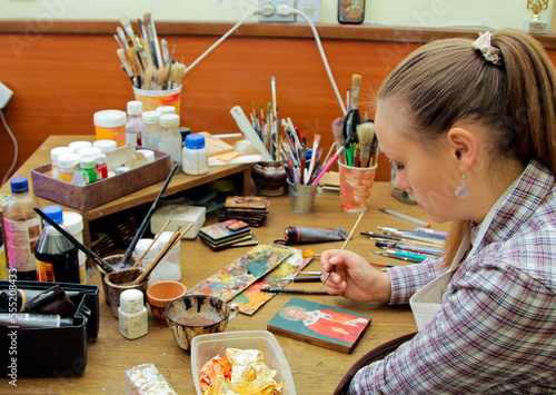 Girl artist paints a picture in the studio. Reproduction of the icon of St. Nicholas. Workflow of the artist in the studio. Brushes and paints on the background art workplace. photo