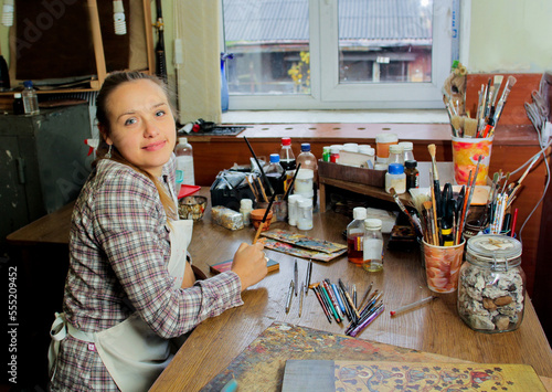 Girl artist paints a picture in the studio.. Smiling in the camera. Reproduction of the icon of St. Nicholas. Workflow of the artist in the studio. Brushes and paints on the background art workplace. photo