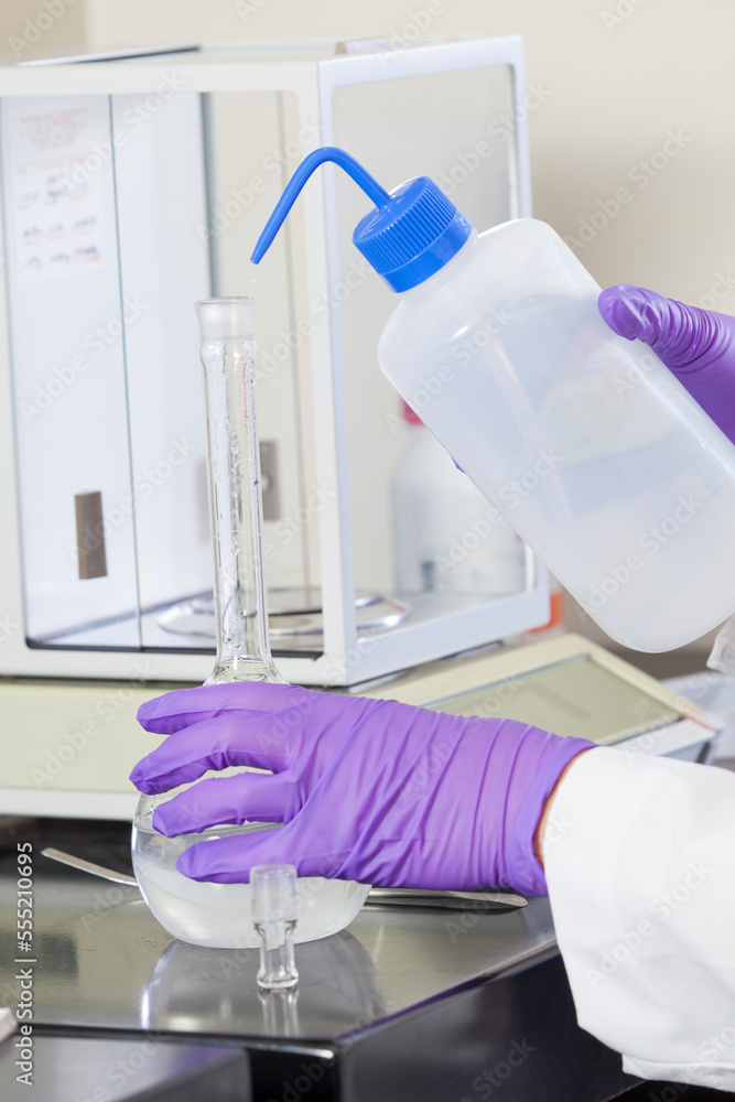 Laboratory scientist washing solid reagent into a water sample in a flask Laboratory scientist washing solid reagent into a water sample in a flask