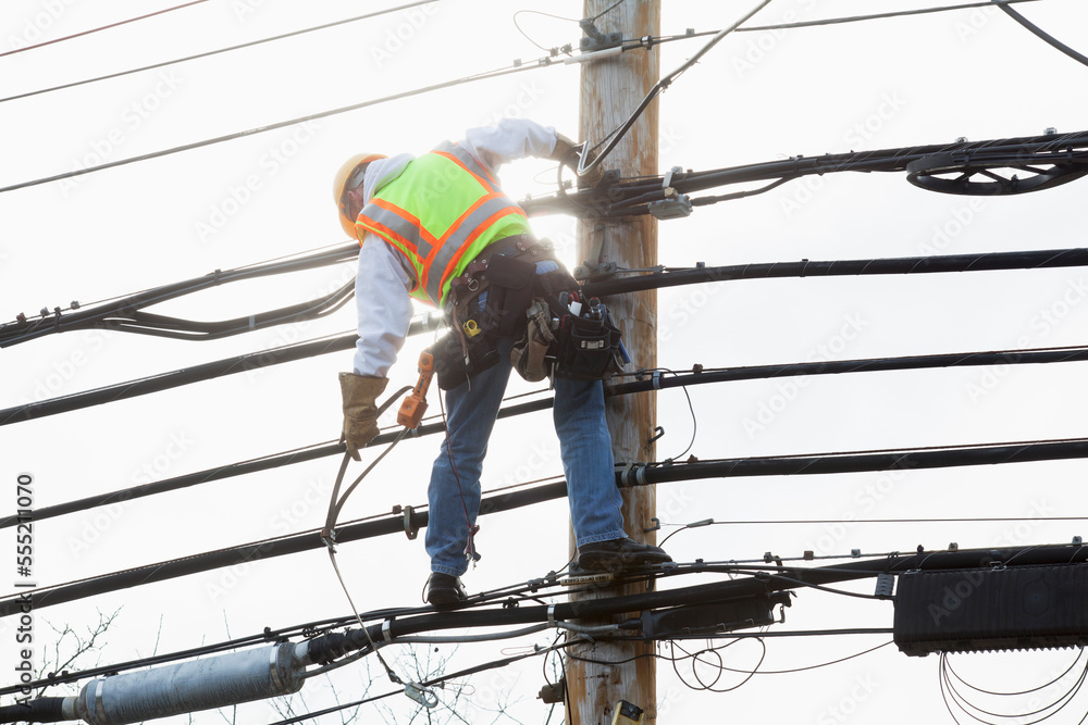 Communications worker on a power pole preparing to strap safety harness to support cable Communications worker on a power pole preparing to strap safety harness to support cable