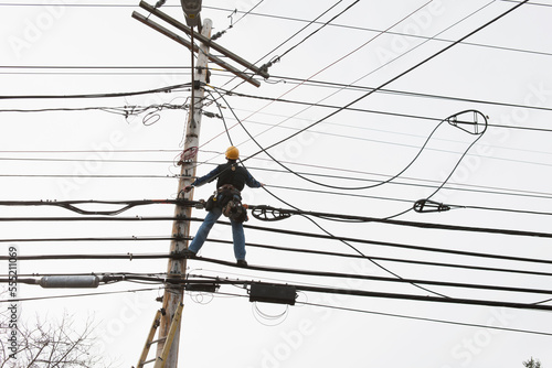 Communications worker on a power pole installing new cable to existing bundles photo