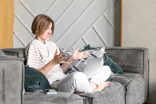 Unhappy woman sits on the couch after working on laptop at home. Distance education and online job concept