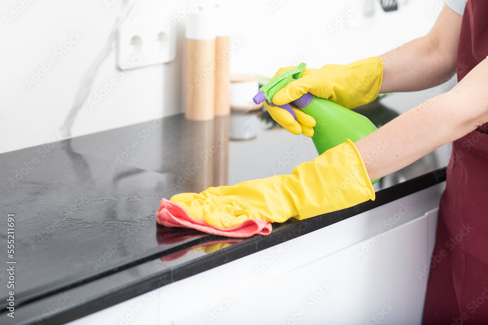 Close up shot of female hands holding bottle spray and rag for cleaning the stove Close up shot of female hands holding bottle spray and rag for cleaning the stove