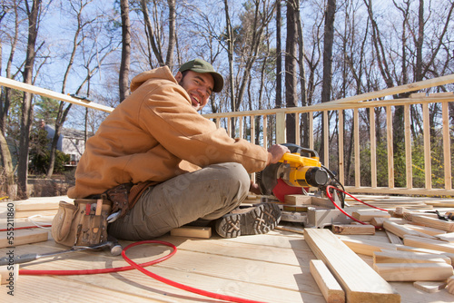 Hispanic carpenter using chop saw to cut deck railing cap photo