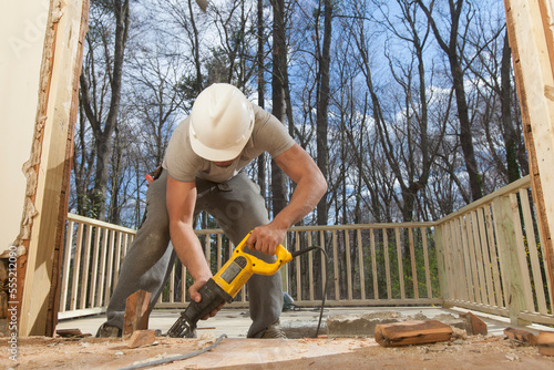 Hispanic carpenter using reciprocating saw to cut framing pieces for removal photo