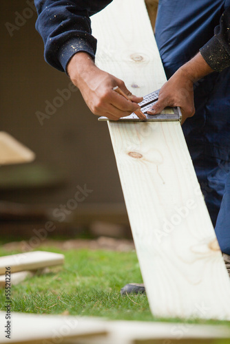 Hispanic carpenter using square to mark cut on board for construction photo