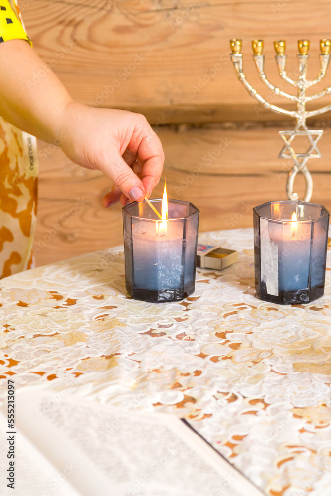 Fototapeta premium The hands of a Jewish woman light candles in honor of Shabbat on the table.