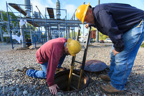 Power engineers placing ladder inside manhole at high voltage power distribution station photo