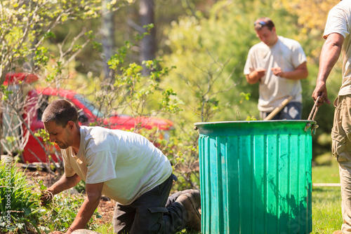 Landscapers clearing weeds from a garden into a bin