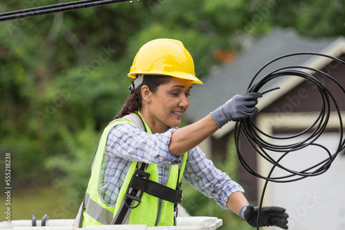 Hispanic female cable lineman stringing a new line in the rain photo