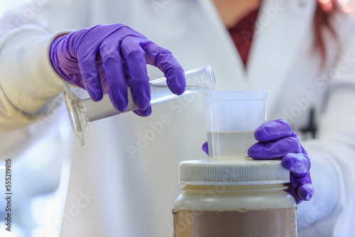 A scientist wearing purple gloves and pouring a solution into a container