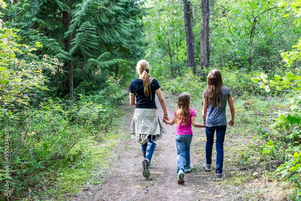 Three sisters holding hands and walking on a trail in a forest; British Columbia, Canada Three sisters holding hands and walking on a trail in a forest; British Columbia, Canada