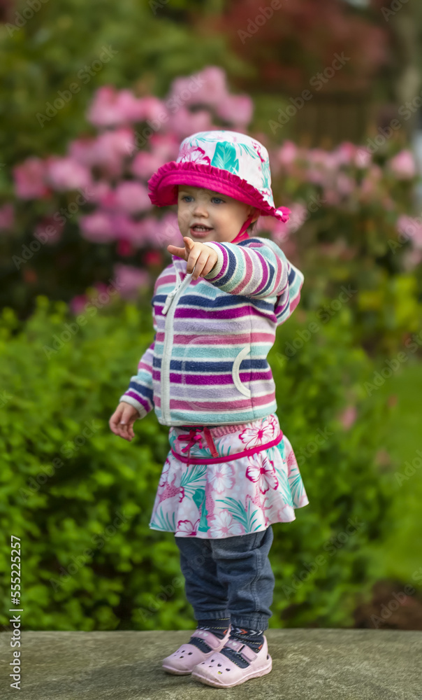 Portrait of young girl standing in the park wearing colorful outfit and pointing at something; Surrey, British Columbia, Canada Portrait of young girl standing in the park wearing colorful outfit and pointing at something; Surrey, British Columbia, Canada
