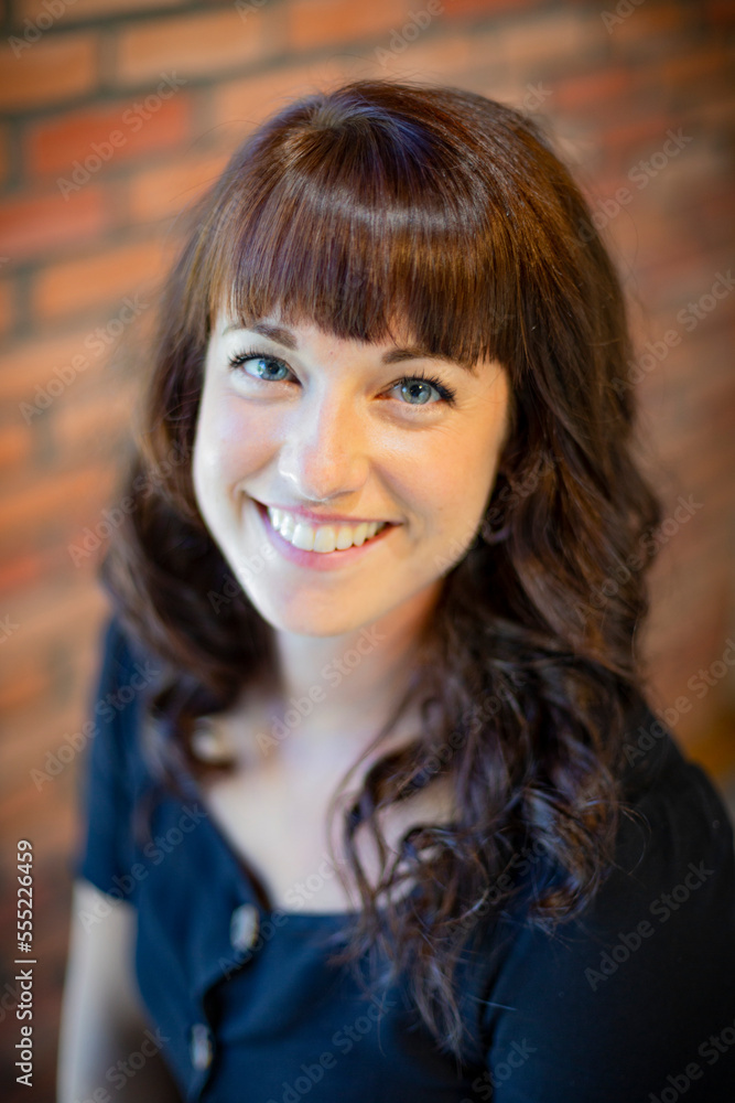 Portrait of a young woman with long brunette hair and blue eyes against a brick wall; Studio Portrait of a young woman with long brunette hair and blue eyes against a brick wall; Studio