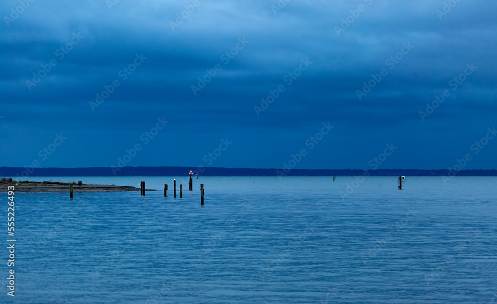 A dark sky covers the coastline and ocean with wooden pilings coming out from shore; British Columbia, Canada A dark sky covers the coastline and ocean with wooden pilings coming out from shore; British Columbia, Canada
