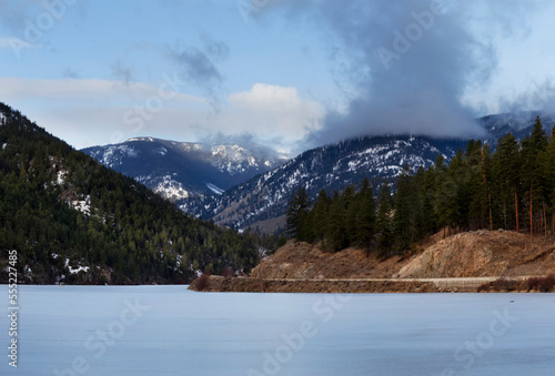 Yellow Lake with a road along the water's edge and clouds over the mountain range, near Olalla, BC; British Columbia, Canada