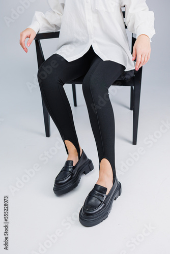 Female beautiful legs in black leather loafers and black leggings. Summer women's shoes