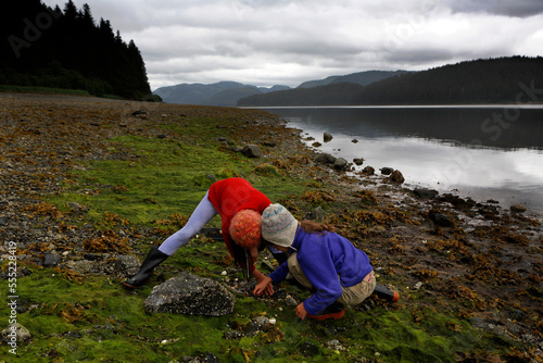 Two girls beach-comb near the water's edge, Inside Passage, Alaska, USA