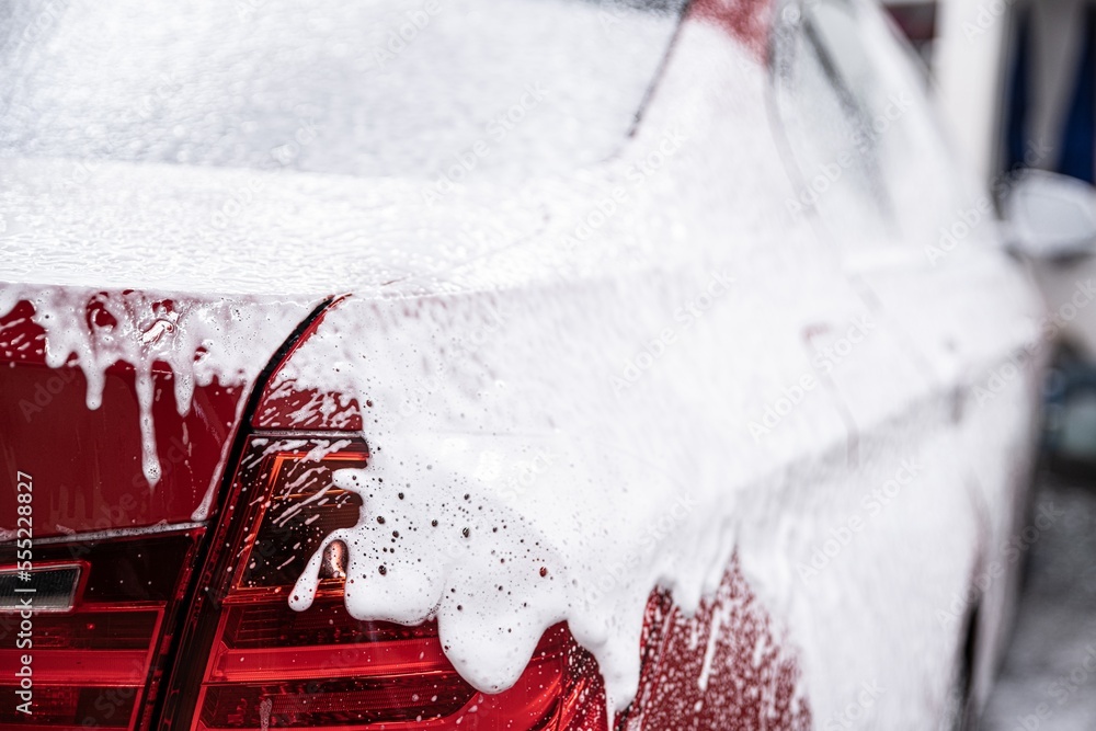 red car covered with white active foam at a manual car wash