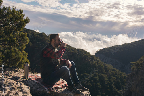 Man with beard taking rest in mountains after walk. Man is drinking hot drinks in mauntains. 
