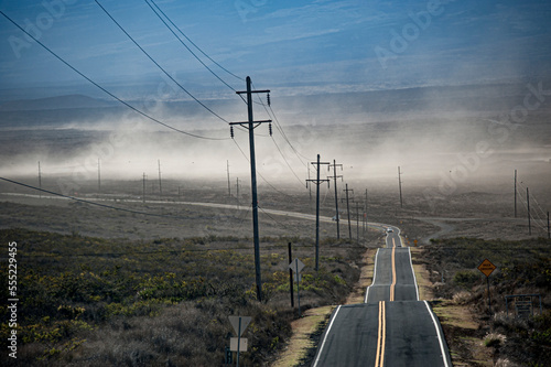 Utility poles line the Saddle Road, which crosses Hawai'i Island (Big Island) from Kona to Hilo and winds whipping up the dust; Hawaii Island, Hawaii, United States of America