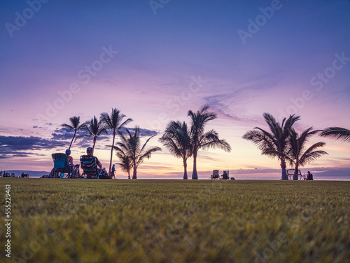 View taken from behind of tourists sitting in lawn chairs watching the sunset over the Pacific coast at Makena; Maui, Hawaii, United States of America photo