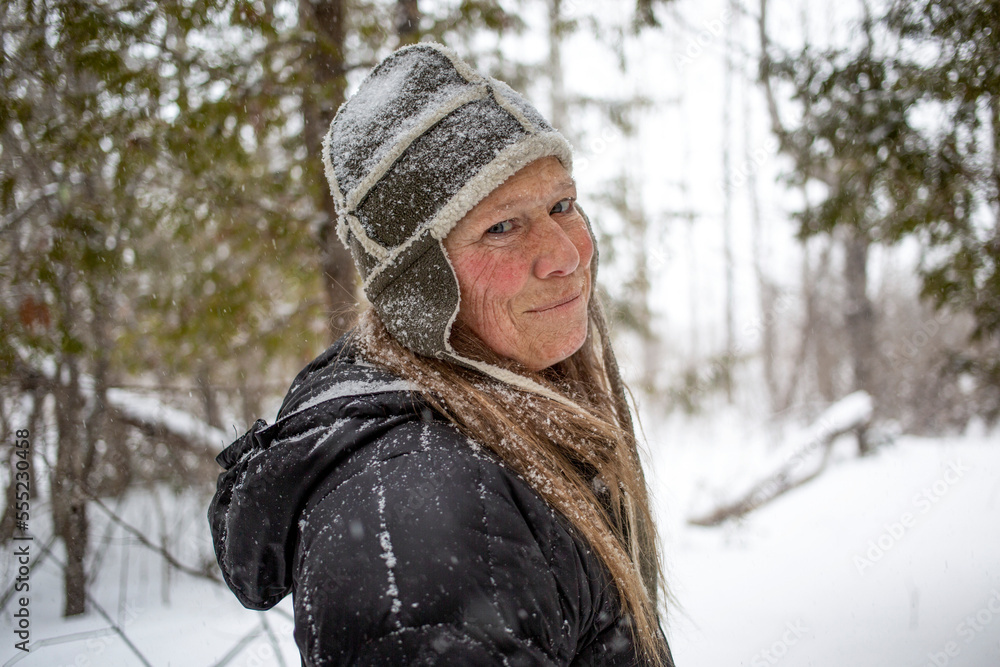 Mature woman enjoying a snowfall in a forest; Ottawa Valley, Ontario, Canada Mature woman enjoying a snowfall in a forest; Ottawa Valley, Ontario, Canada